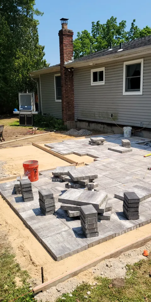 Gray pavers being laid next to a brick chimney, pallets of pavers on the base