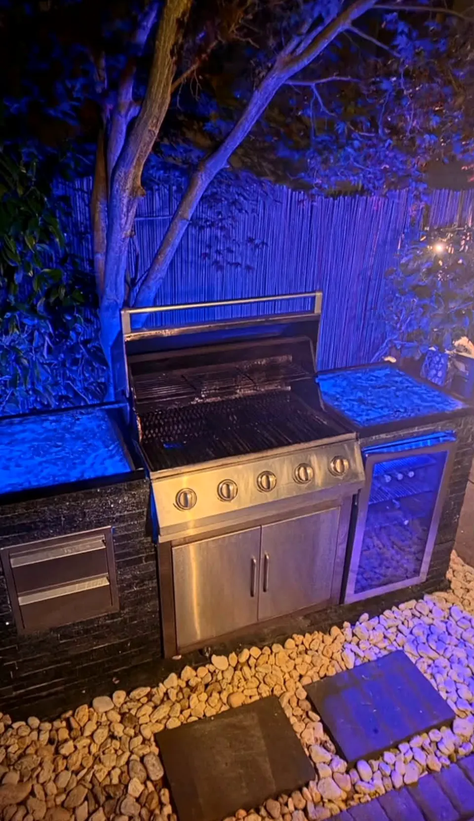 Built-in grill in a stone outdoor kitchen lit at night