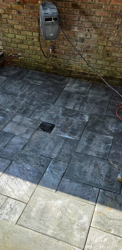 New dark paver landing with a floor drain beside the brick wall